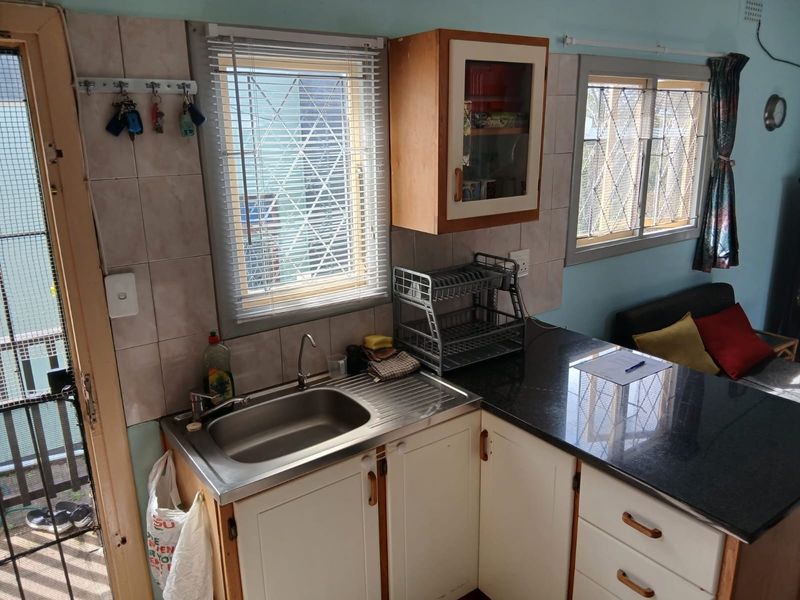 Compact kitchen area featuring granite countertops, stainless steel sink, and built-in cabinetry with tiled backsplash and security-fitted windows.