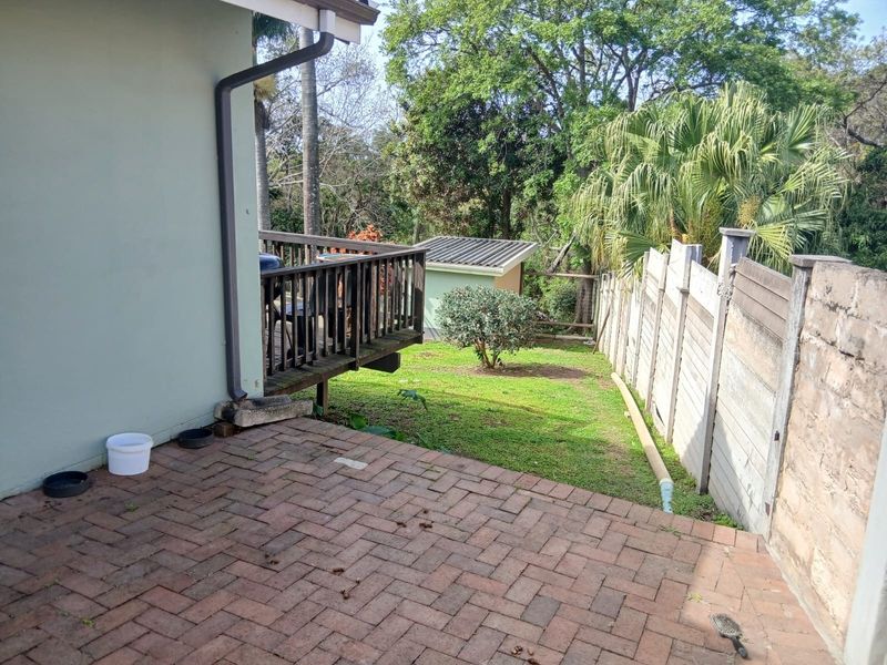 Rear exterior view featuring a brick paved patio, a raised timber deck, and a garden area enclosed by a precast concrete boundary wall.