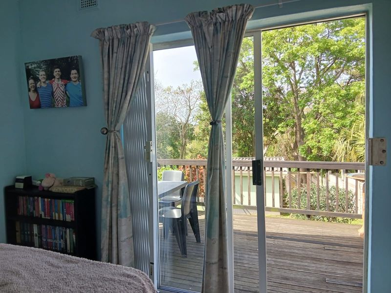 Bedroom featuring a sliding glass door that opens onto an elevated timber deck with a balustrade and garden views.