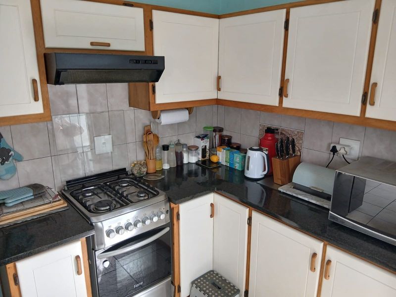 A functional kitchen featuring built-in cabinetry, granite countertops, a tiled backsplash, and a gas stove with an integrated extractor fan.