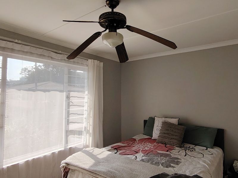 A bedroom featuring a ceiling fan and a large window with security bars, providing natural light and ventilation.