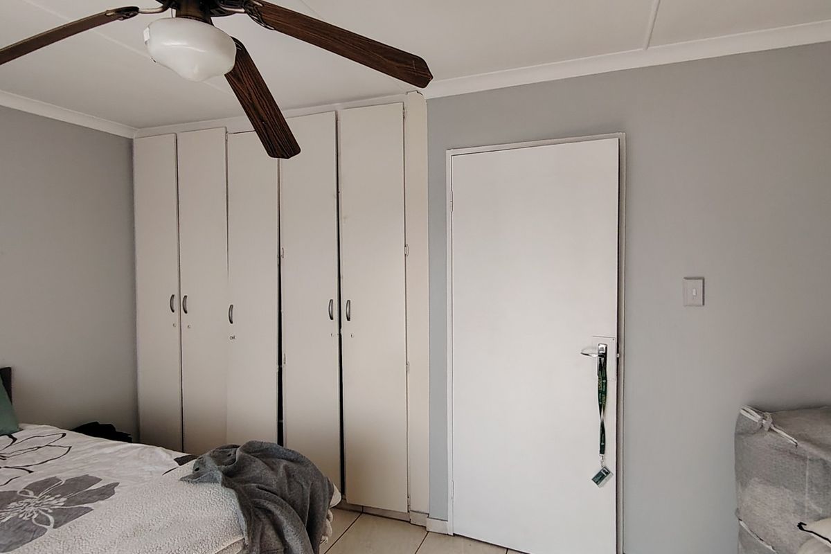 A bedroom featuring built-in cupboards, a ceiling fan, and tiled flooring, providing a functional and neutral living space.