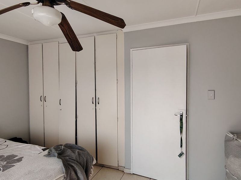 A bedroom featuring built-in cupboards, a ceiling fan, and tiled flooring, providing a functional and neutral living space.