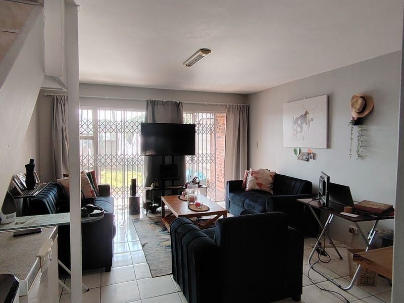 A comfortable living room featuring tiled flooring, a staircase, and a sliding glass door that provides access to the outdoor area.