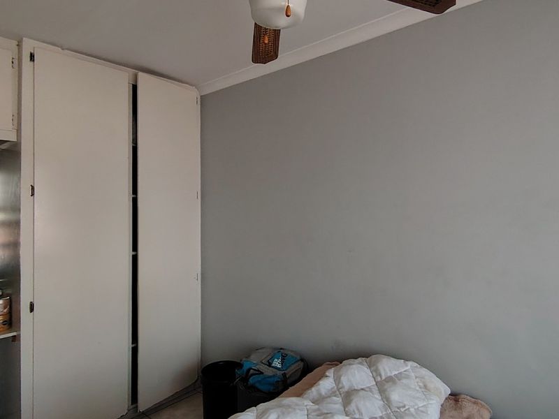A bedroom featuring built-in cupboards and a ceiling fan, offering a functional space with neutral wall finishes.