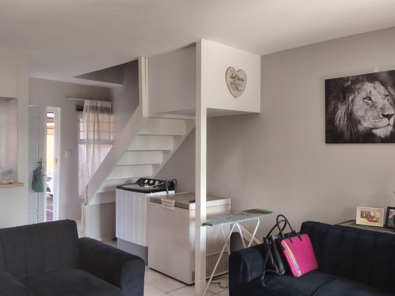Open plan living area featuring tiled flooring, a central staircase, and a breakfast bar connecting to the kitchen space.