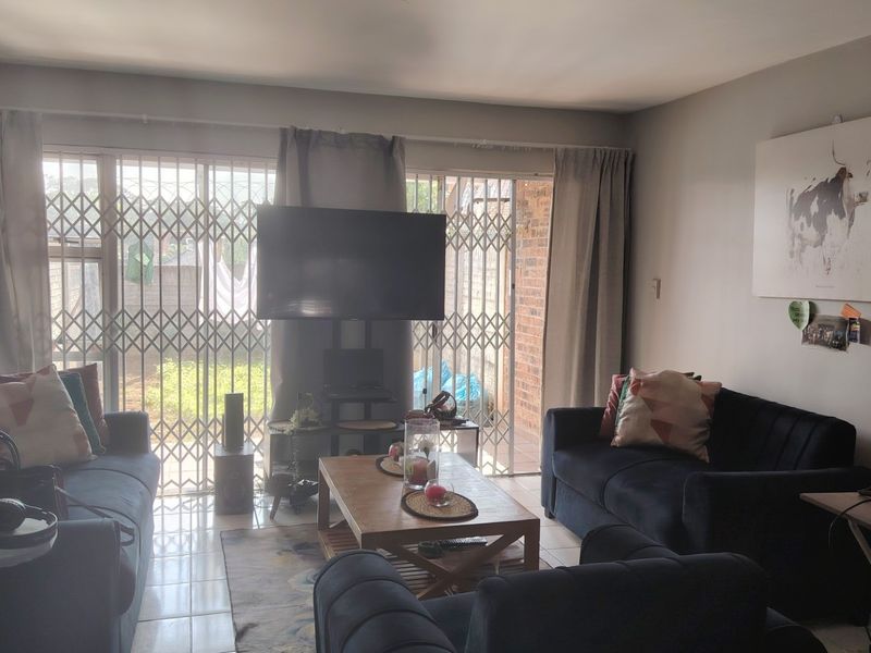 A comfortable living room featuring tiled flooring and large sliding glass doors with security gates, providing direct access to the outdoor area.