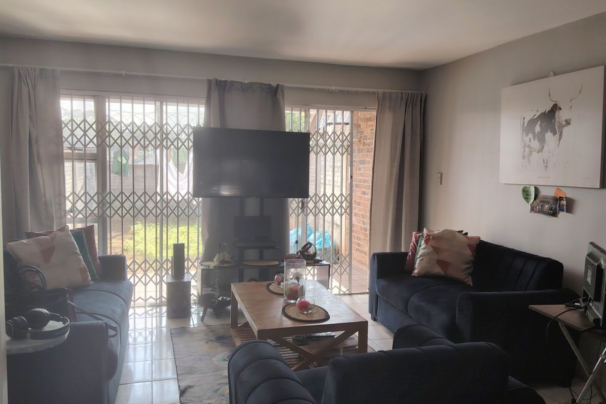 A comfortable living room featuring tiled flooring and large sliding glass doors with security gates, providing direct access to the outdoor area.