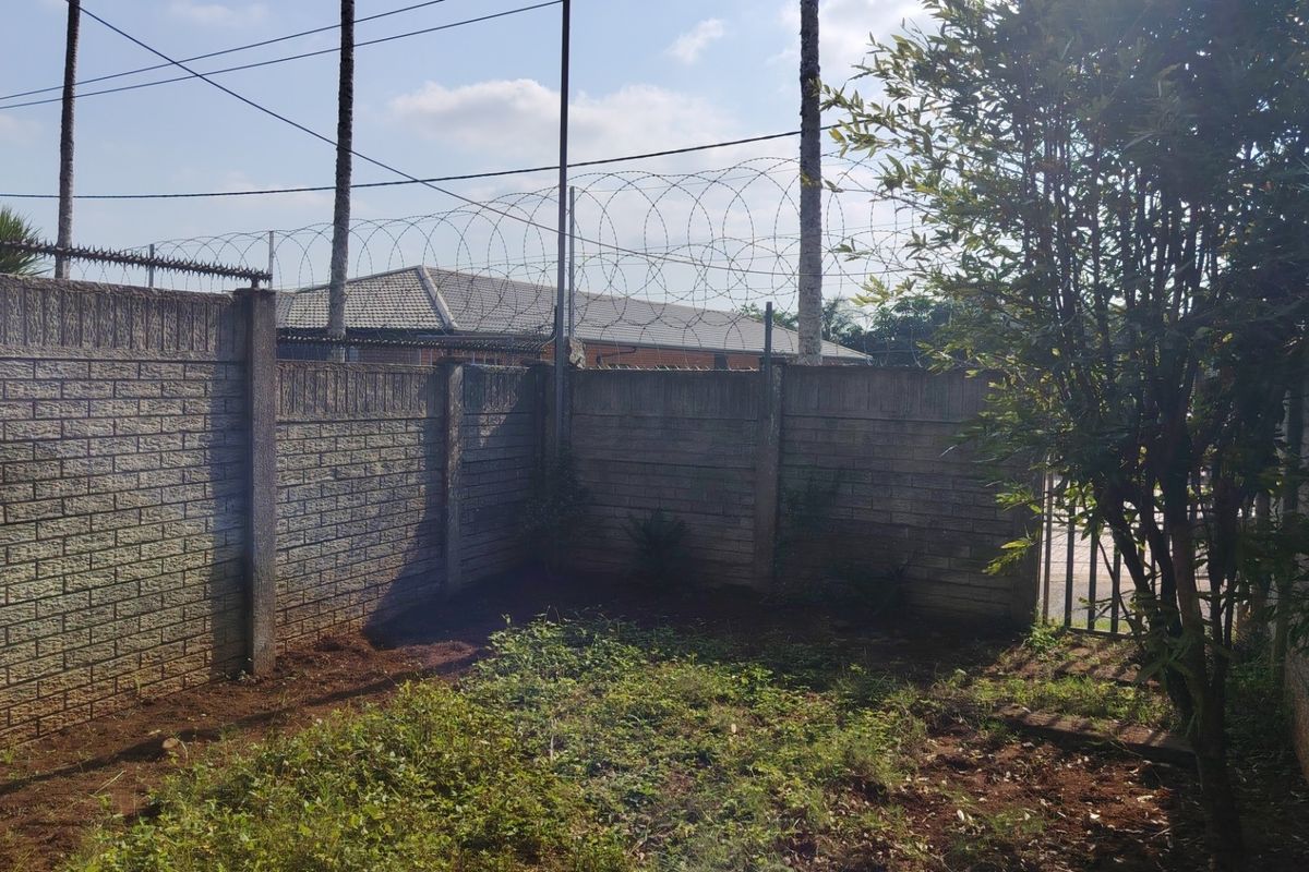A rear garden area enclosed by a precast concrete boundary wall topped with razor wire fencing and featuring a metal gate.