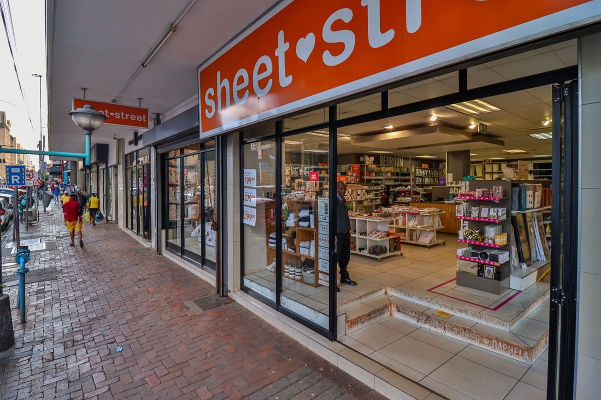 Commercial storefront featuring a glass facade, prominent signage, and a tiled entrance step located on a brick-paved street.
