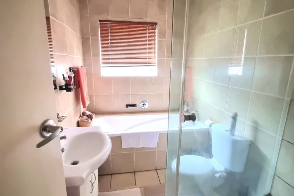 A functional bathroom featuring a built-in bathtub, glass-enclosed shower, pedestal basin, and toilet with neutral wall and floor tiling.