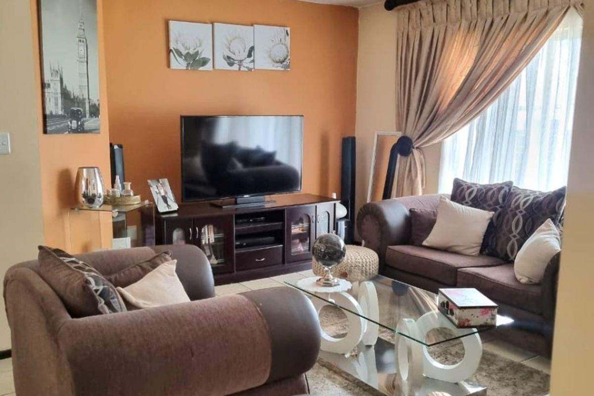 A comfortable living room featuring tiled flooring and large windows with curtain rails, providing a functional and inviting space.
