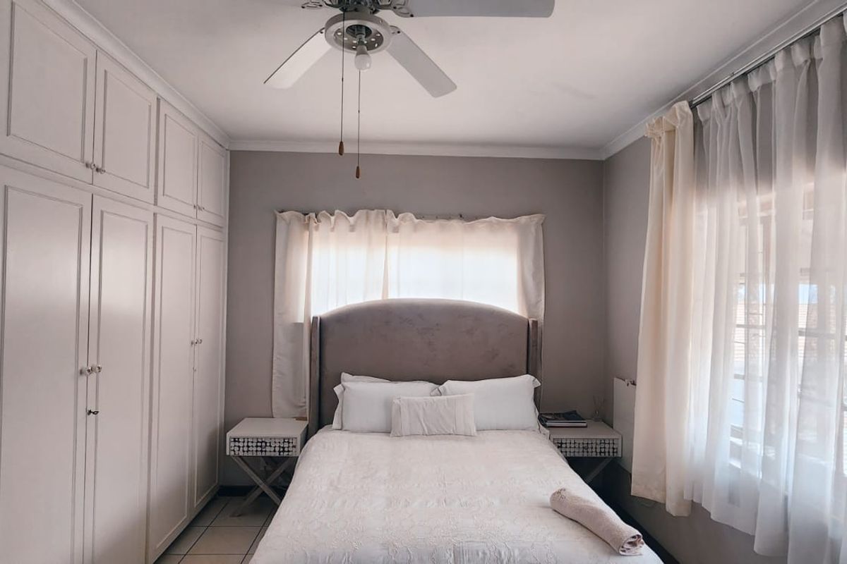 A well-maintained bedroom featuring extensive built-in cupboards, a ceiling fan, and tiled flooring, offering a clean and functional living space.