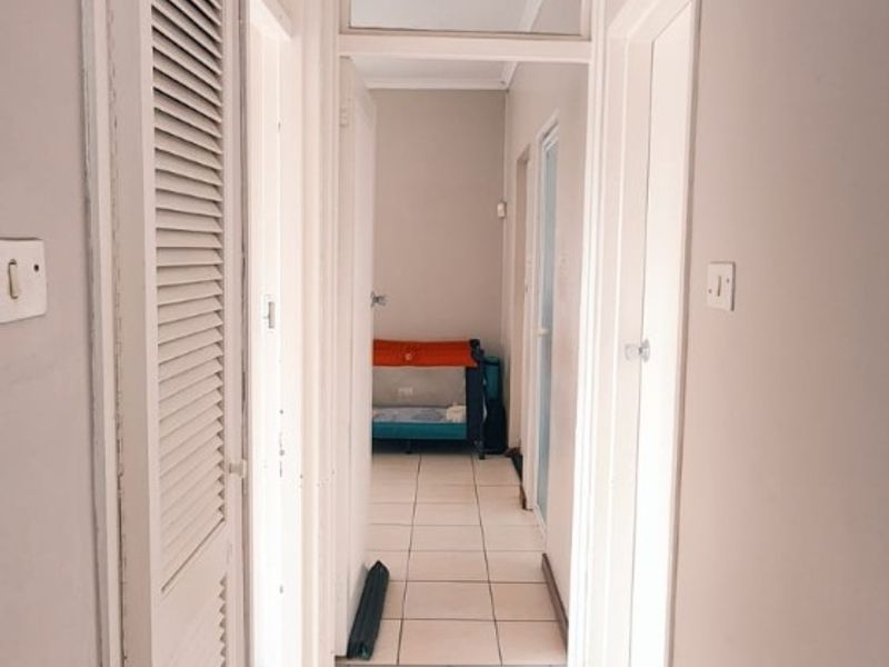 A functional apartment hallway featuring tiled flooring, louvered closet doors, and a ceiling access hatch, providing access to multiple rooms.