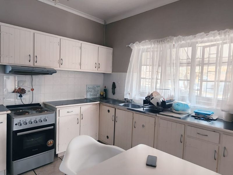A functional kitchen featuring white built-in cabinetry, laminate countertops, a tiled backsplash, and a freestanding stove with an extractor fan.