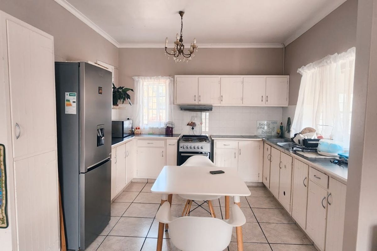A functional kitchen featuring white built-in cabinetry, tiled flooring, a tiled backsplash, and a freestanding stove with an extractor fan.