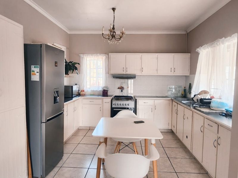 A functional kitchen featuring white built-in cabinetry, tiled flooring, a tiled backsplash, and a freestanding stove with an extractor fan.