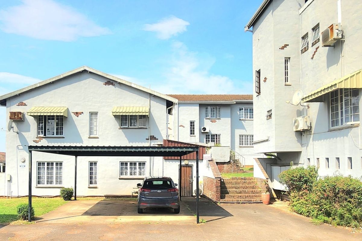 Rear view of the apartment complex featuring a paved driveway, covered carport, and external brick staircase access to the units.