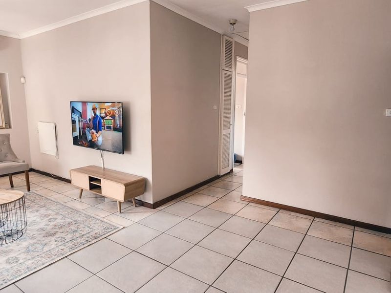 A living room featuring neutral wall tones, tiled flooring, an air conditioning unit, and a built-in storage cupboard.