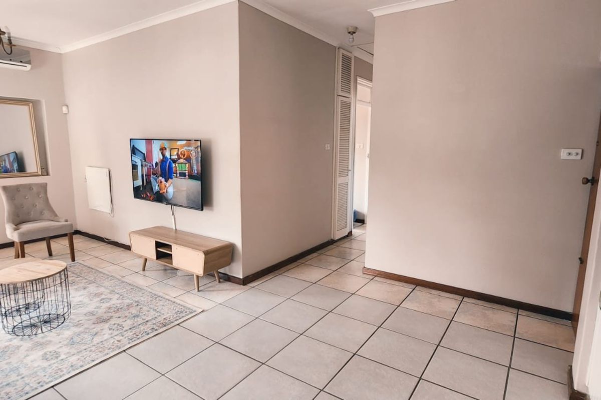 A living room featuring neutral wall tones, tiled flooring, an air conditioning unit, and a built-in storage cupboard.