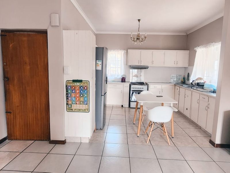 Open-plan kitchen and living area featuring tiled flooring, white cabinetry, and a functional layout with a central dining space.
