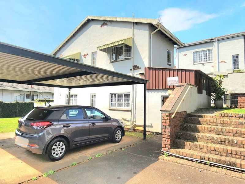 Exterior view of the apartment building featuring a covered carport, brick staircase, and paved driveway area.
