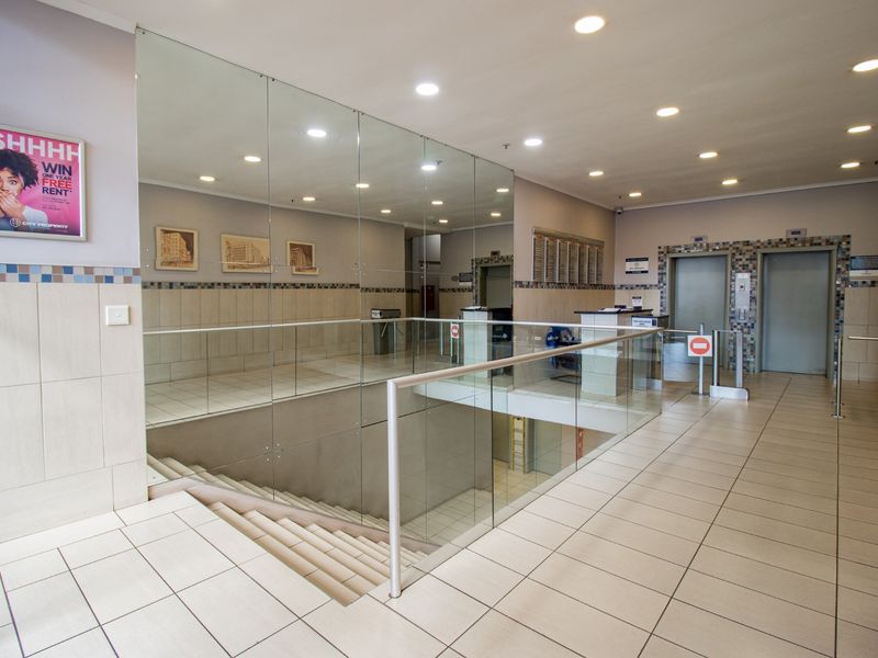 A modern commercial building lobby featuring tiled flooring, glass balustrades, security turnstiles, and elevator access.