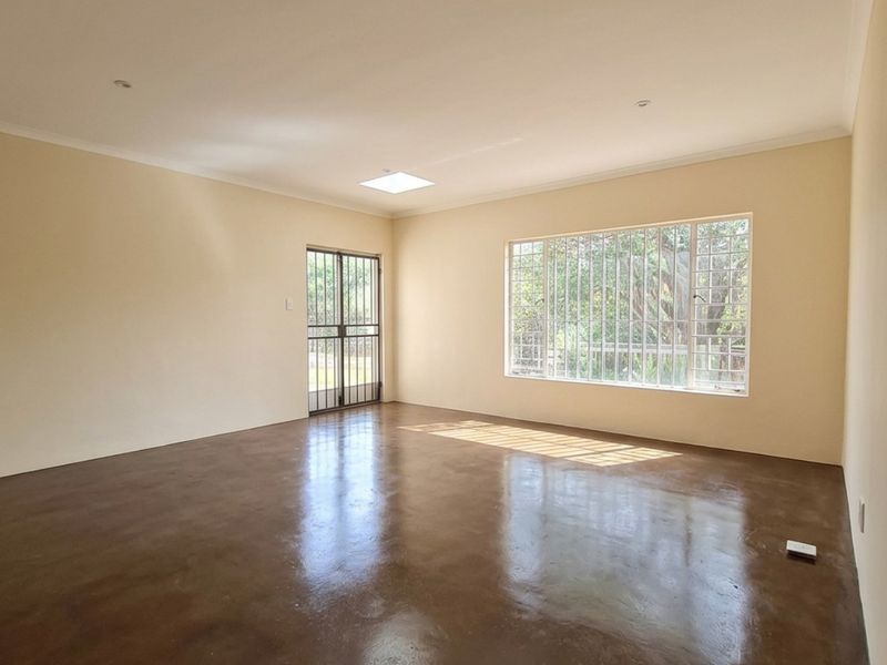 A spacious, empty living area featuring polished concrete floors, a skylight, and large windows with security bars, offering a bright and clean blank canvas.
