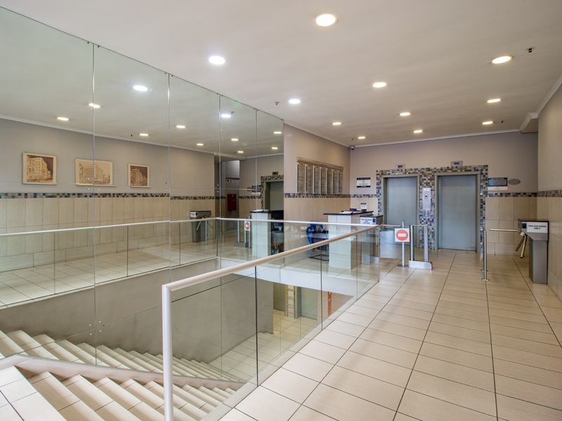 A professional commercial building lobby featuring tiled floors, a glass balustrade, mirrored walls, security turnstiles, and elevator access.