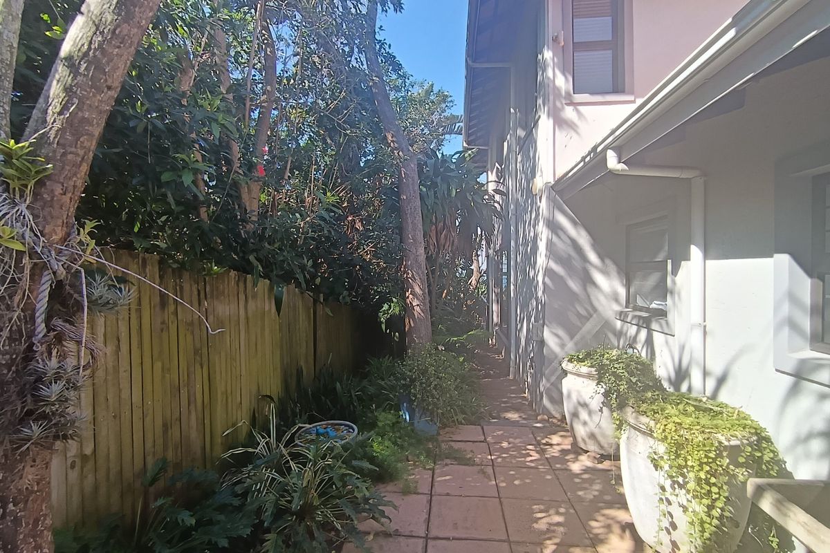 A side pathway along the rear of the property featuring paved flooring, a timber boundary fence, and established garden landscaping.