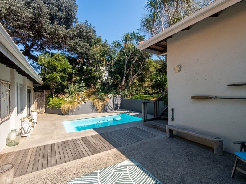 A private outdoor pool area featuring a concrete patio, timber decking, and a landscaped garden setting with a retaining wall.