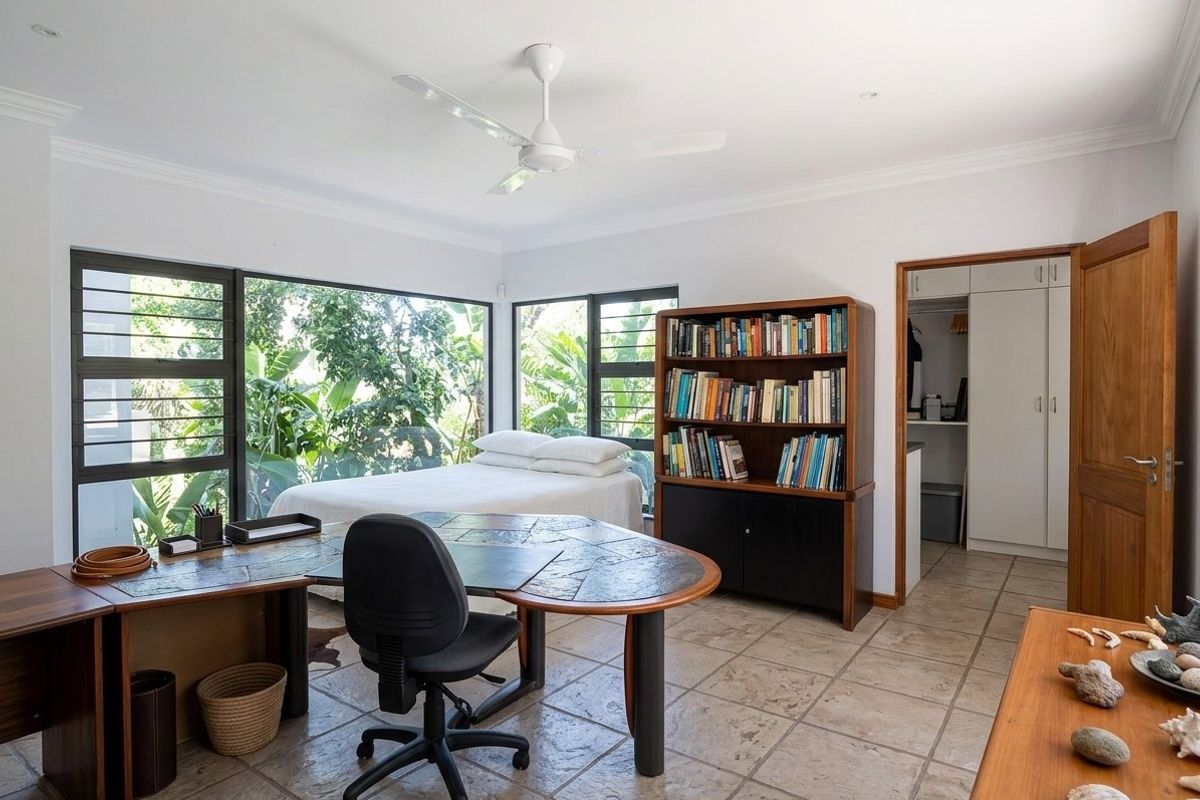 A spacious bedroom featuring large corner windows with garden views, tiled flooring, a ceiling fan, and a built-in wardrobe.
