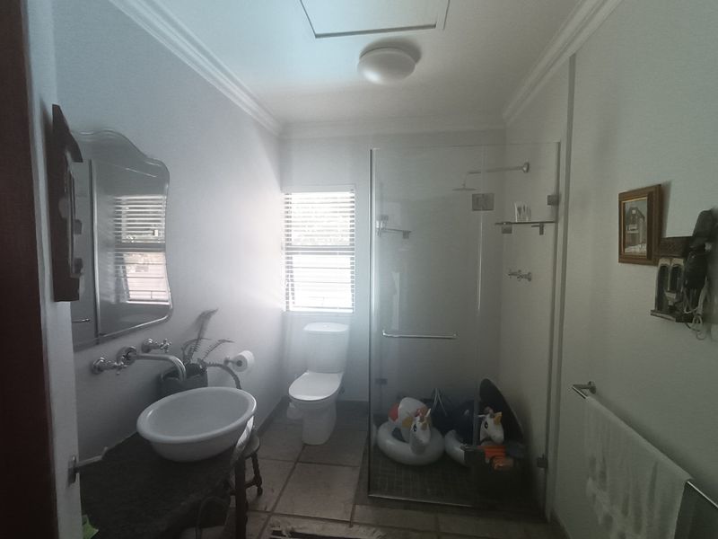 A functional bathroom featuring a vessel sink with wall-mounted tap, stone vanity, and a modern glass-enclosed shower with a rain shower head.