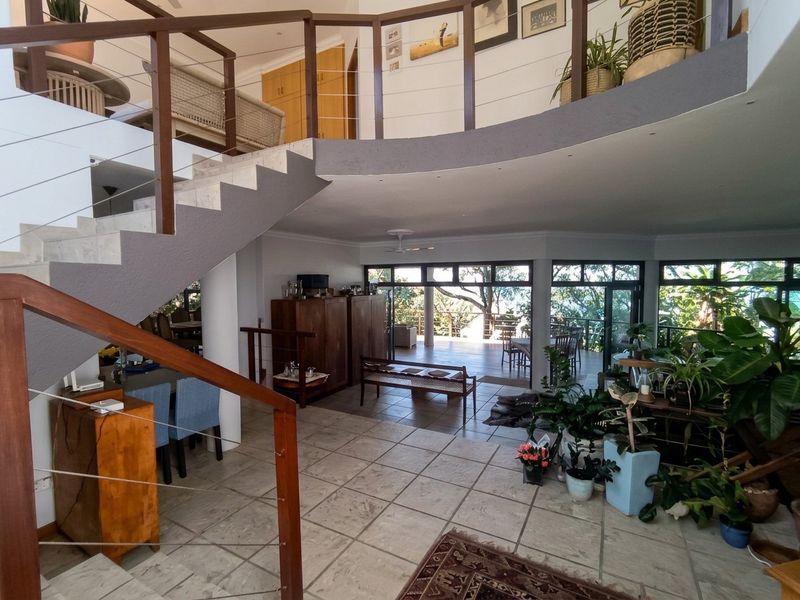 Spacious open-plan living area featuring a prominent staircase with timber handrails, tiled flooring, and large sliding glass doors leading to an outdoor deck.