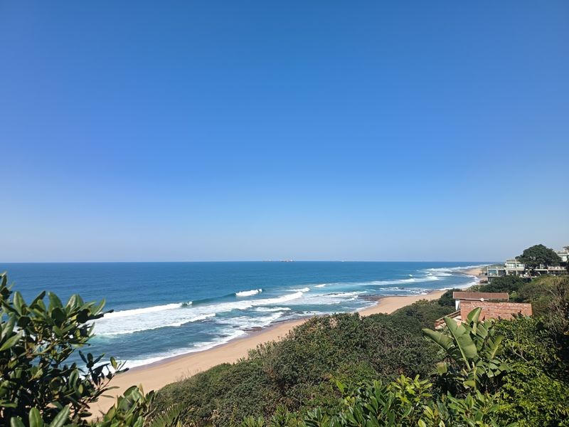 A scenic elevated view overlooking the coastline, sandy beach, and ocean, showcasing the property's prime coastal location.