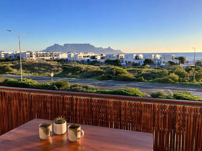 A scenic elevated view overlooking the coastal landscape, road, and Table Mountain, featuring a balcony with a bamboo privacy screen.