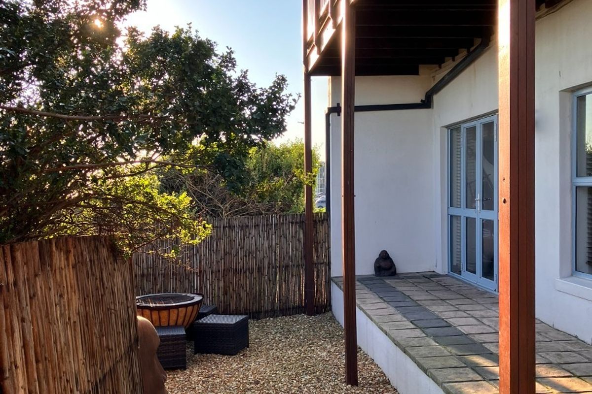 Rear exterior view of the townhouse featuring a paved patio, timber balcony overhead, artificial lawn, and bamboo privacy fencing.