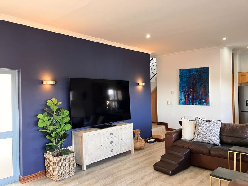 A well-maintained living room featuring a bold navy accent wall, recessed downlighting, and modern laminate flooring, creating a contemporary and inviting atmosphere.