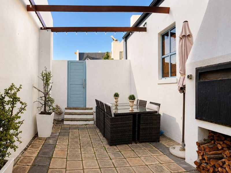 A private courtyard patio featuring a built-in braai, timber pergola overhead, and paved flooring, providing a functional outdoor entertainment space.
