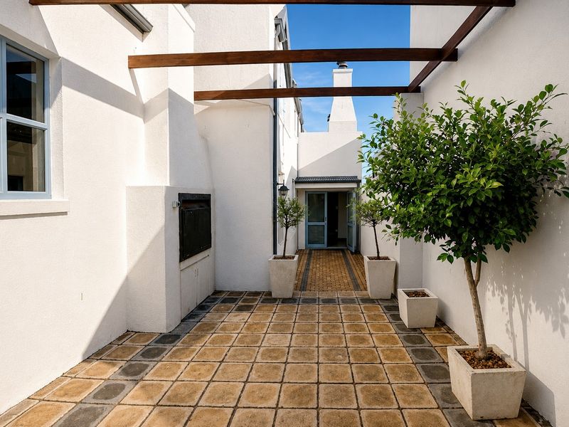 A well-maintained outdoor patio area featuring a built-in braai, timber pergola, and paved flooring, providing a clean and functional space for outdoor entertaining.