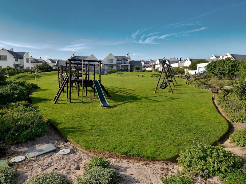 A well-maintained communal garden area featuring a green lawn and playground equipment, situated within a residential townhouse complex.