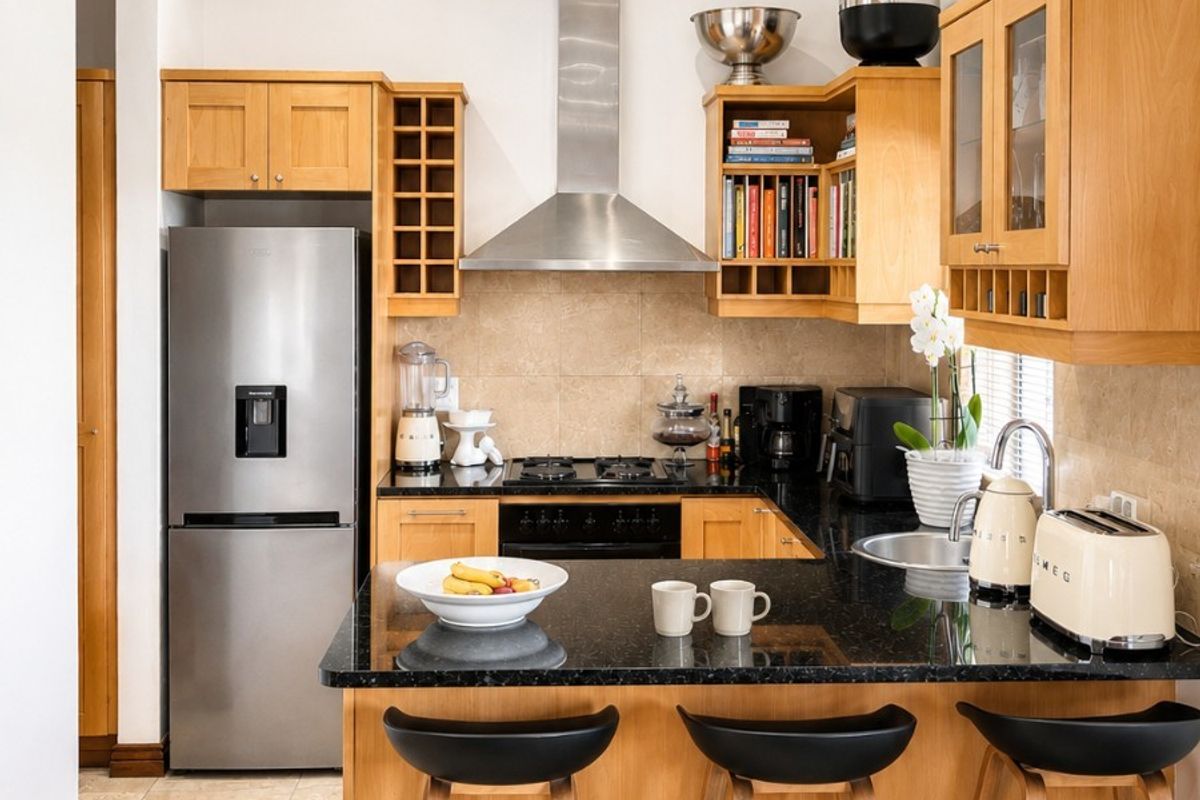 A well-maintained kitchen featuring wooden cabinetry, granite countertops, a gas hob, and stainless steel appliances, complemented by neutral tiled flooring and recessed lighting.