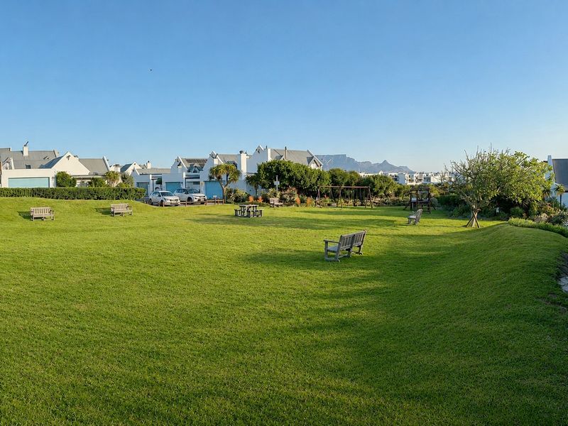 A well-maintained communal garden area featuring expansive green lawns, mature landscaping, and mountain views in the background.