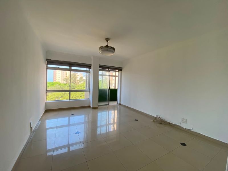 A bright, empty living room featuring polished tiled floors, a ceiling fan, and large windows with access to a balcony.