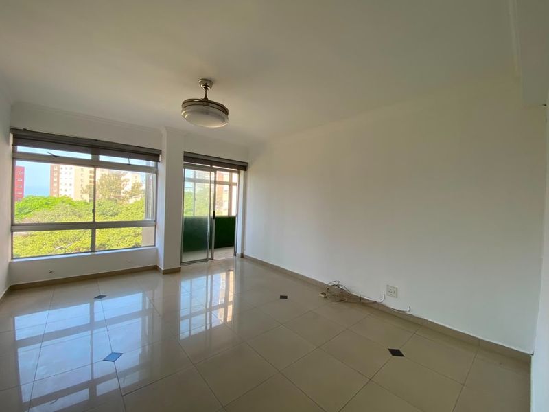 A bright, empty living room featuring tiled floors, a ceiling fan, and large windows with access to a balcony.