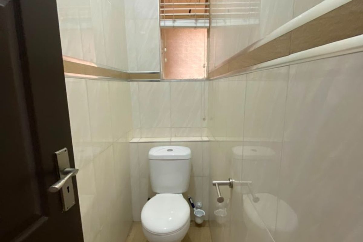 A compact, fully tiled guest bathroom featuring a modern toilet, neutral wall tiles with decorative accents, and a small window for ventilation.