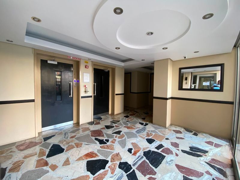 A well-maintained apartment building lobby featuring decorative terrazzo flooring, recessed ceiling lighting, and dual elevator access.