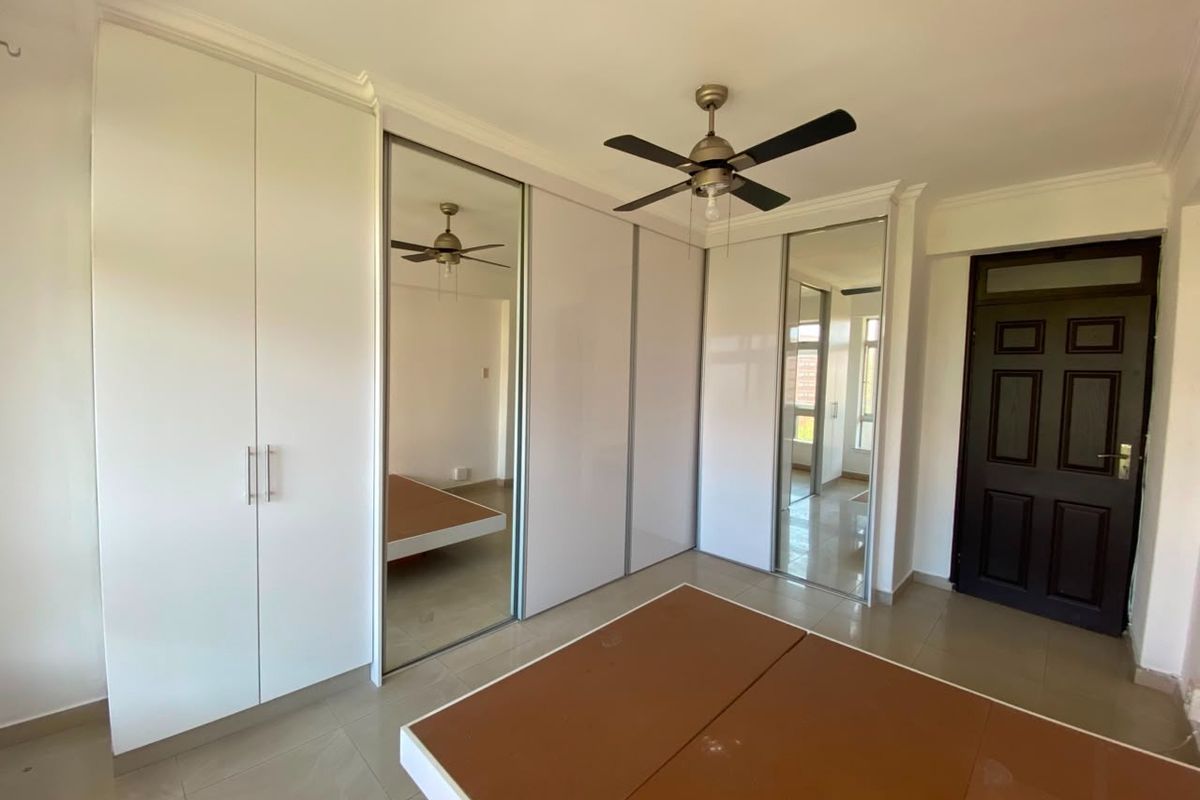 Spacious bedroom featuring extensive built-in cupboards with mirrored doors, a ceiling fan, and neutral tiled flooring.
