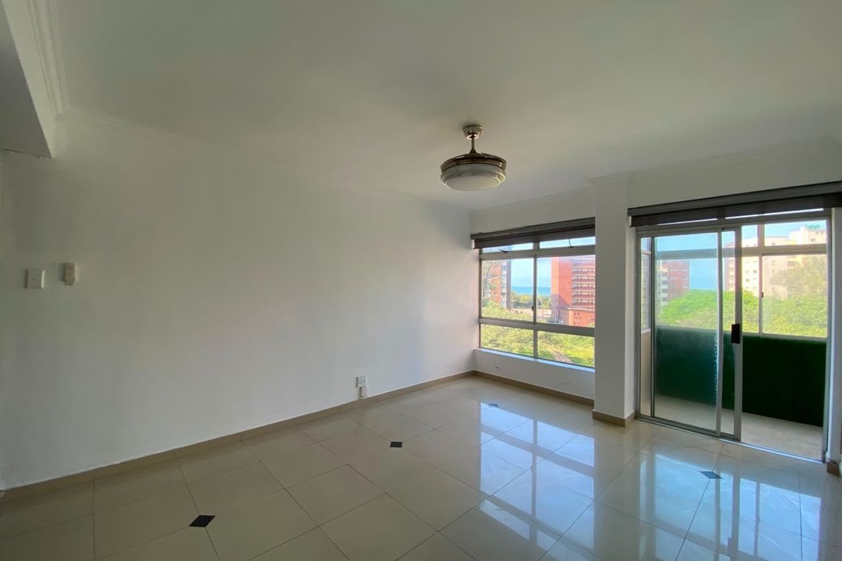 A bright, empty living area featuring tiled floors, a ceiling fan, and large windows with access to an adjoining balcony.