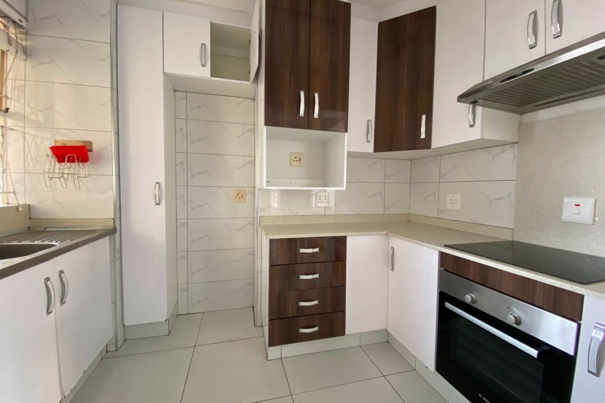 Modern kitchen featuring two-tone cabinetry, stone countertops, built-in oven, electric hob, extractor fan, and tiled finishes throughout.